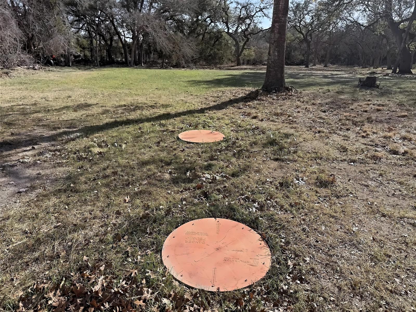 Two septic access lids set in the grass with oaks in the background